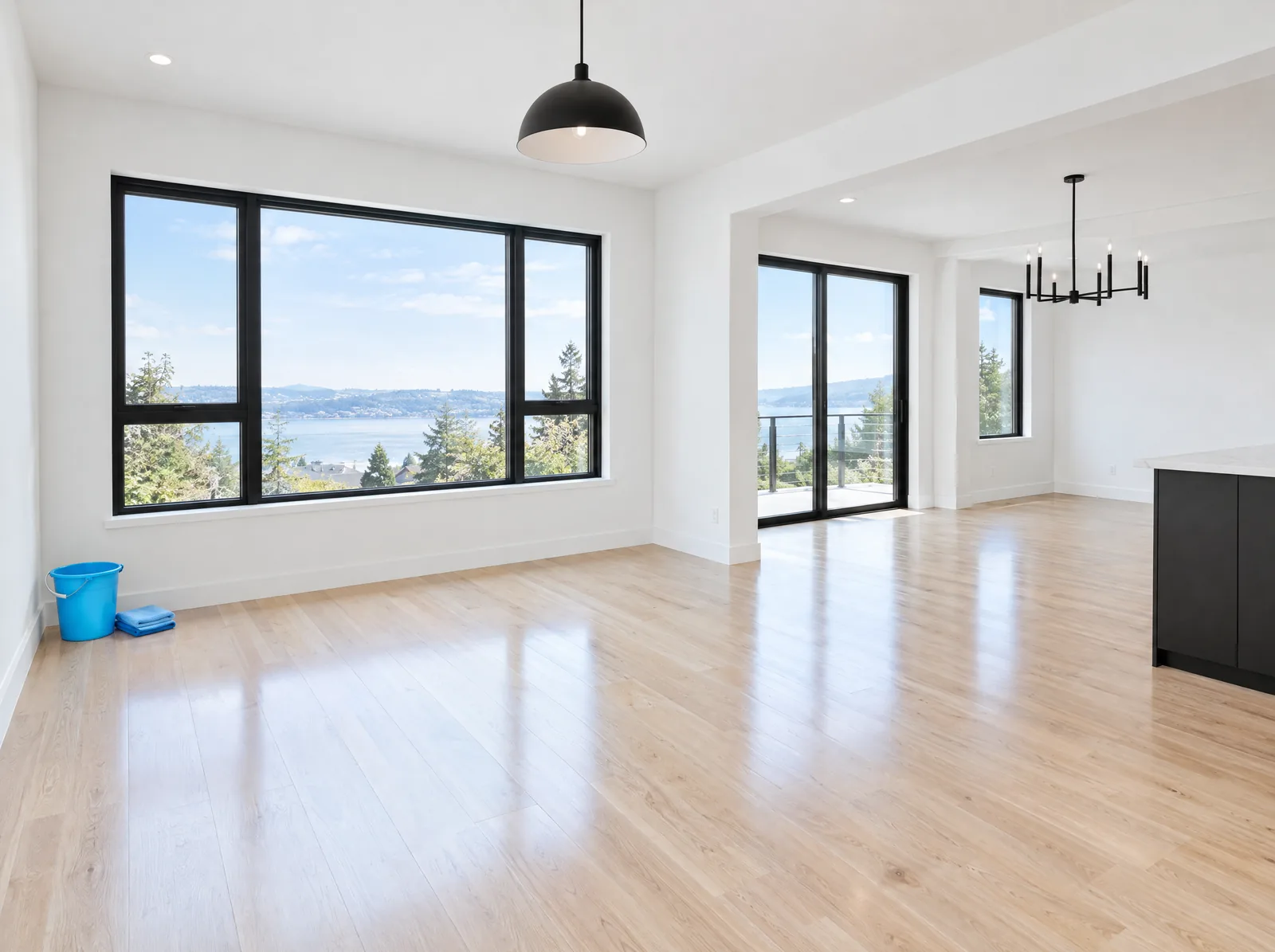 Newly finished room with light wood floors, large black-framed windows and a blue bucket with cloths.